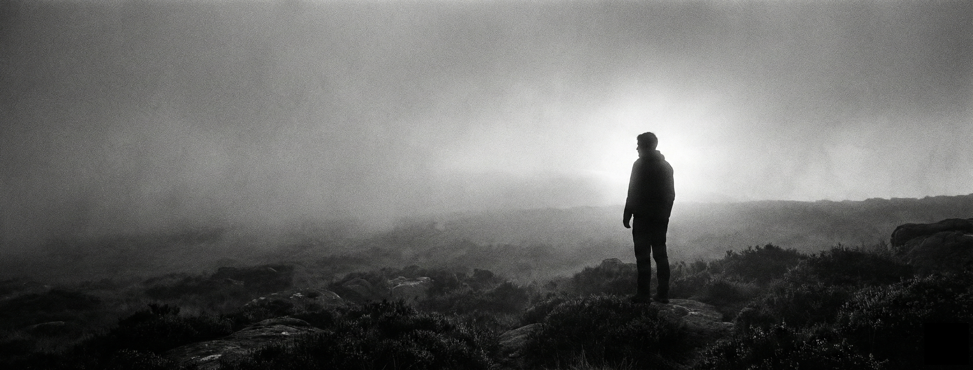 深い霧が立ち込める荒野に佇み、遠くを見つめる人物のモノクロ写真